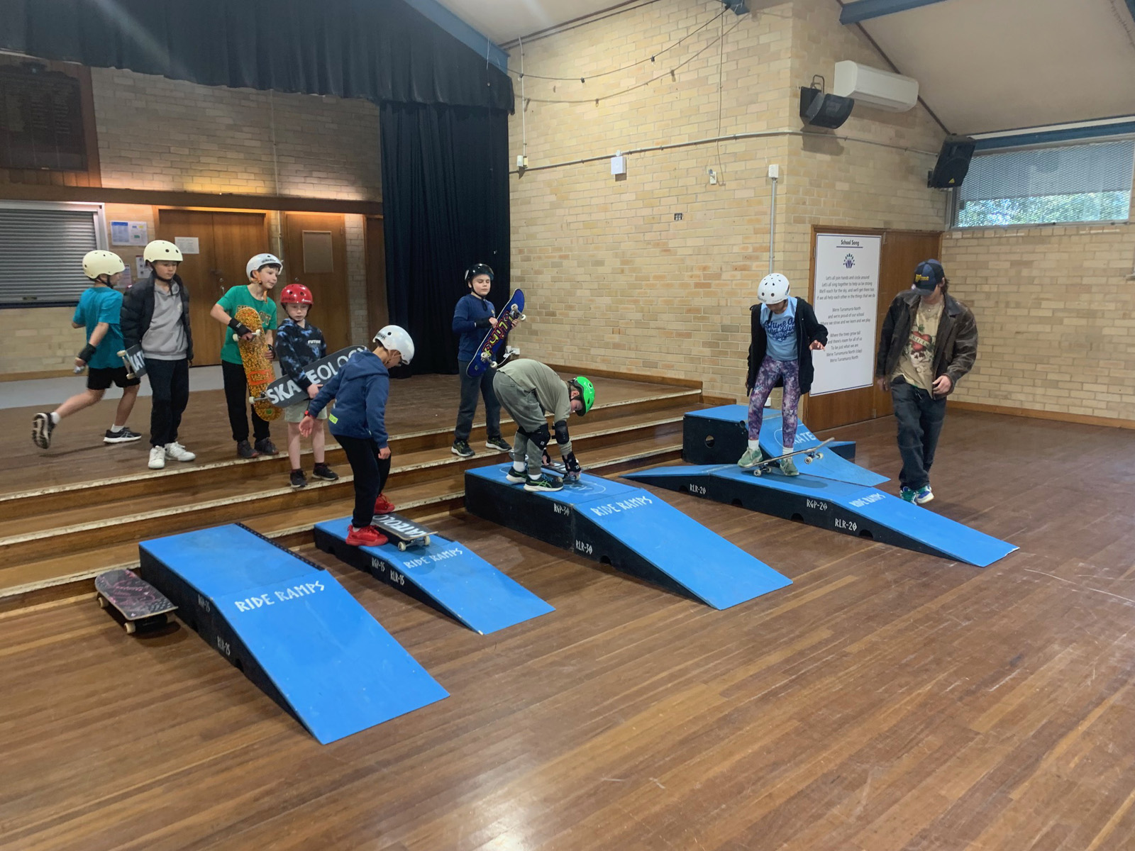 Kids at vacation care skateboarding inside school hall.
